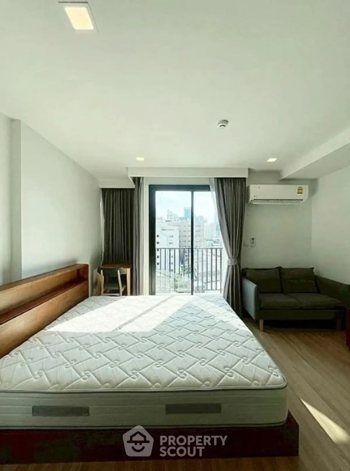 Bright bedroom with large window and city view, featuring a cozy sofa and modern decor.
