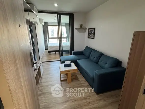 Modern living room with blue sofa and wooden flooring, open view to bedroom