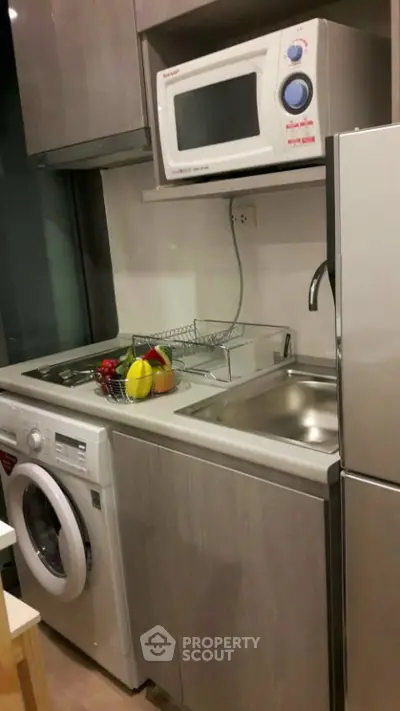 Compact kitchen with modern appliances including washing machine, microwave, and stainless steel sink.