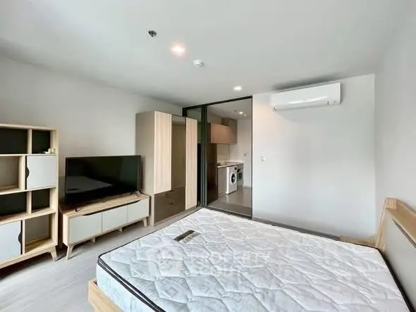 Modern bedroom with TV, air conditioning, and view into kitchen with washing machine.
