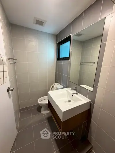 Modern bathroom with sleek fixtures and neutral tiles, featuring a large mirror and compact layout.
