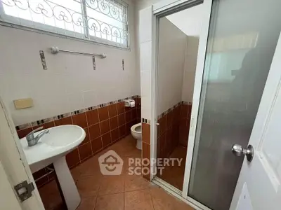Compact bathroom with shower and pedestal sink, tiled walls and floor.