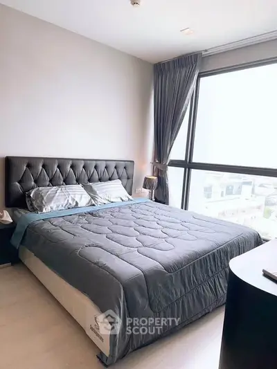 Modern bedroom with large window and stylish decor in a high-rise apartment.