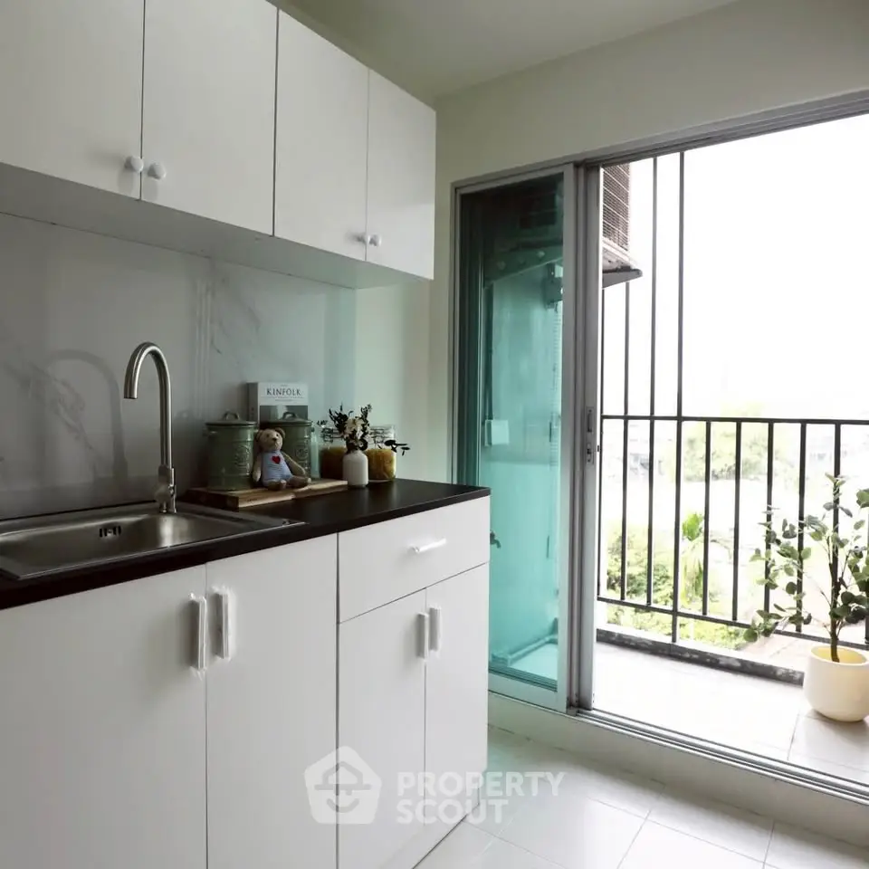 Modern kitchen with sleek white cabinets and balcony access, offering a bright and airy atmosphere.