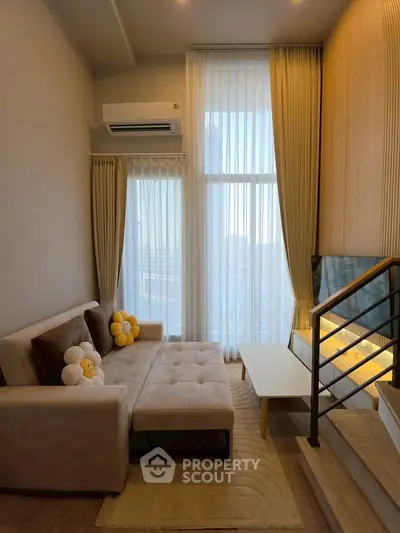 Modern living room with high ceilings, cozy sofa, and large windows offering city views.