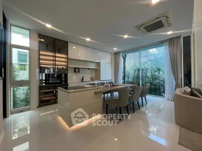 Luxurious modern kitchen with open layout and dining area, featuring sleek cabinetry and large windows.