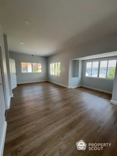 Spacious and well-lit living room with elegant hardwood flooring and multiple windows offering ample natural light, perfect for family gatherings.