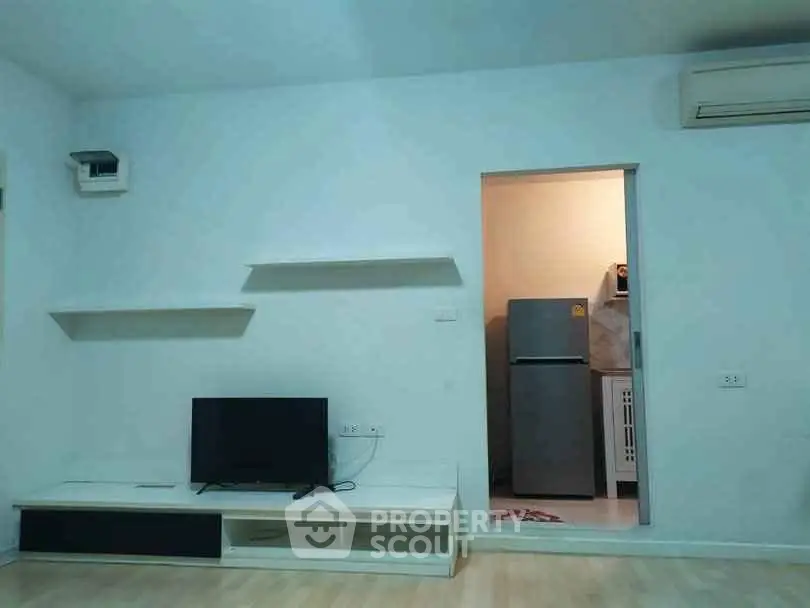 Modern living room with minimalist decor and adjacent kitchen area featuring a refrigerator.