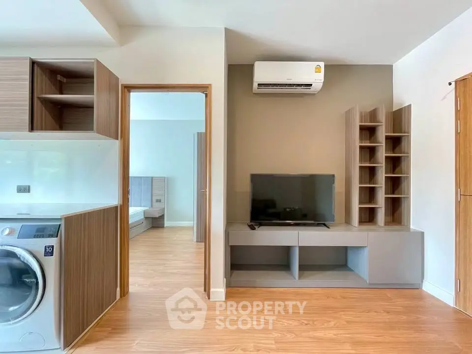 Modern apartment interior with open layout, featuring a washing machine, TV, and air conditioning.