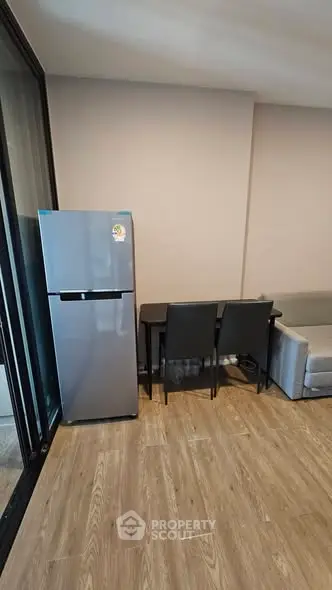 Modern apartment interior with fridge, dining table, and sofa on wooden flooring.
