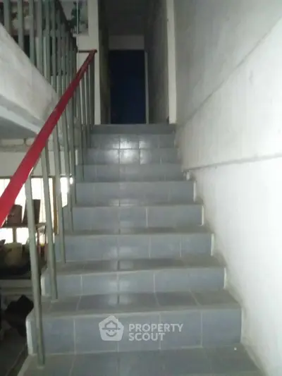 Dimly lit staircase in a residential building with tiled steps and metal railing.