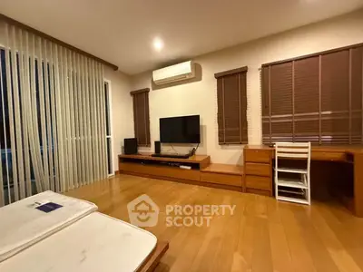 Spacious living room with wooden flooring and modern furniture, featuring a large TV and air conditioning.