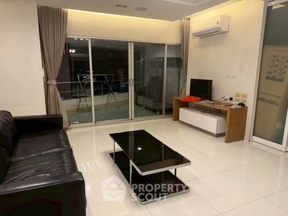 Modern living room with sleek black sofa, glass coffee table, and balcony view in a stylish apartment.