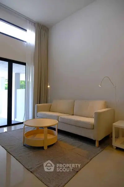 Modern living room with high ceiling and large windows, featuring a cozy sofa and stylish coffee table.