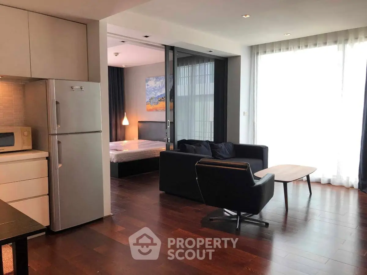 Modern open-plan living room with sleek kitchen and cozy bedroom area, featuring stylish furniture and natural light.