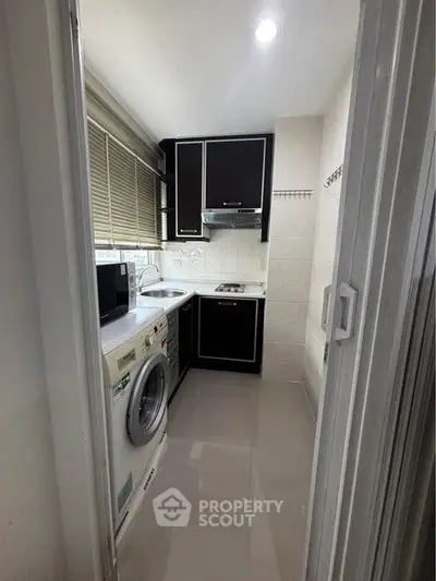 Compact kitchen with modern appliances and sleek black cabinets in a cozy apartment.