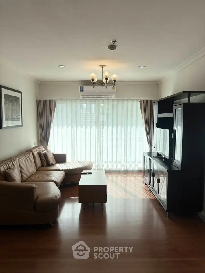 Spacious living room with leather sofa and entertainment unit, featuring large windows and elegant lighting.
