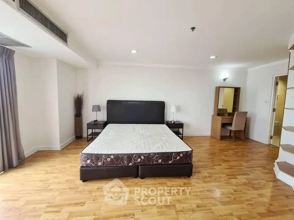 Spacious bedroom with wooden flooring and modern furnishings in a luxury apartment.