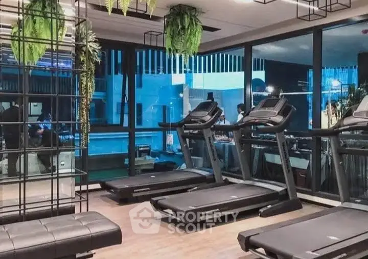 Modern gym with treadmills and large windows overlooking a pool area.