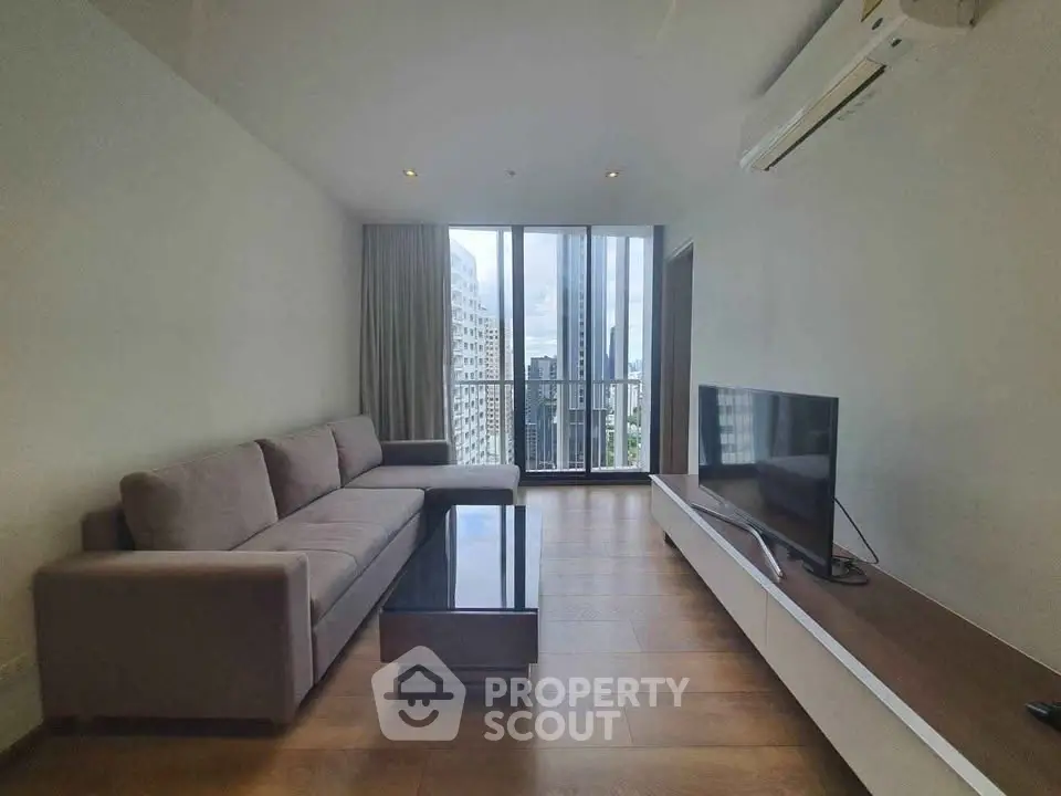 Modern living room with large windows and city view, featuring sleek furniture and air conditioning.