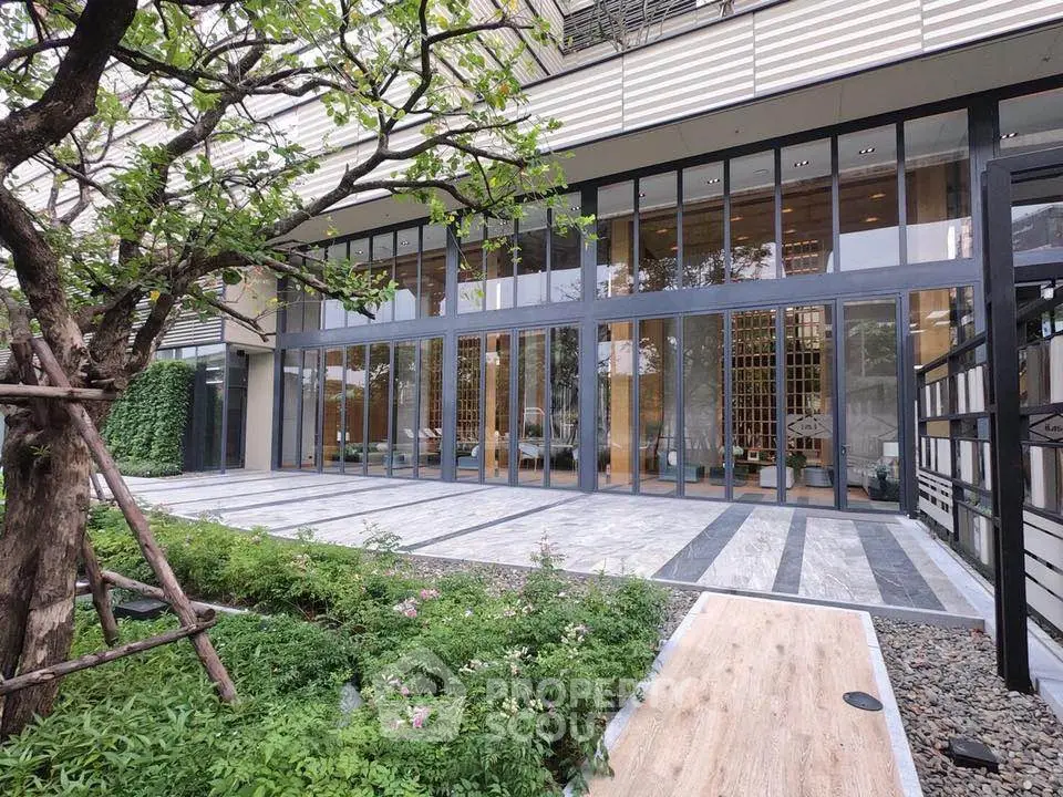 Modern building entrance with large glass windows and lush greenery