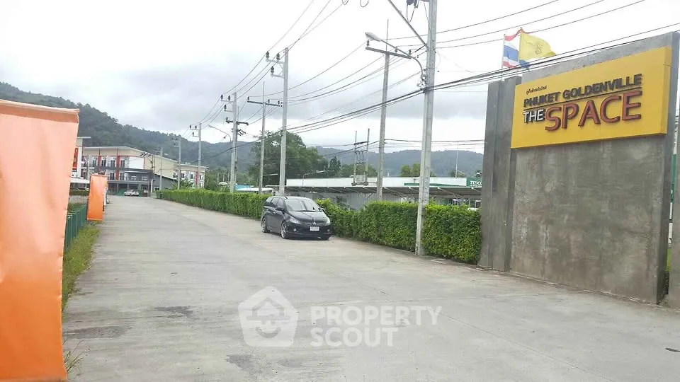 Entrance to commercial property with signage and parking area, surrounded by lush greenery and mountain views.