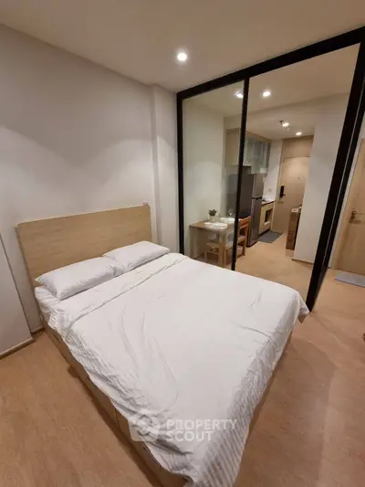 Modern bedroom with wooden flooring and glass partition leading to kitchen area