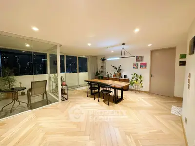 Spacious modern living room with elegant wooden flooring and large glass doors leading to a balcony with city views.