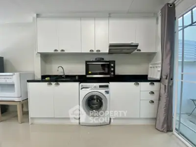 Modern kitchen with washing machine and microwave, sleek white cabinets, and black countertops.