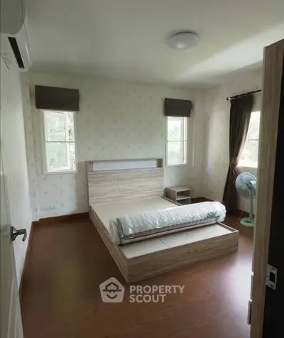 Cozy bedroom with wooden flooring and natural light from two windows