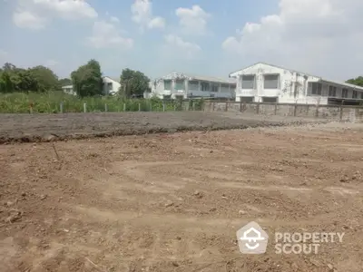 Expansive vacant land ready for development, showcasing potential with a backdrop of modern white residential structures under a clear sky.