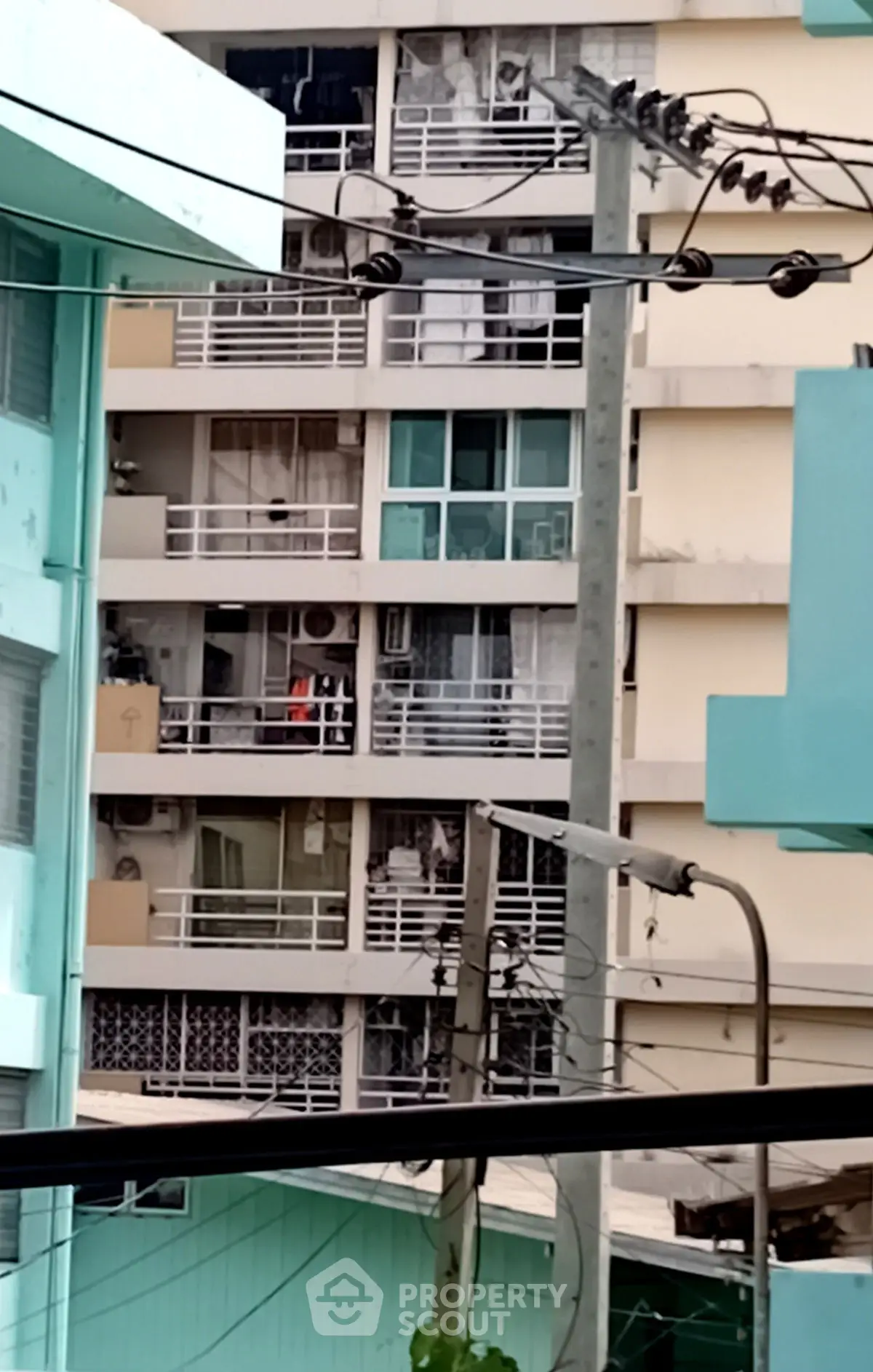 Urban apartment building exterior with multiple balconies and electrical wires in view.