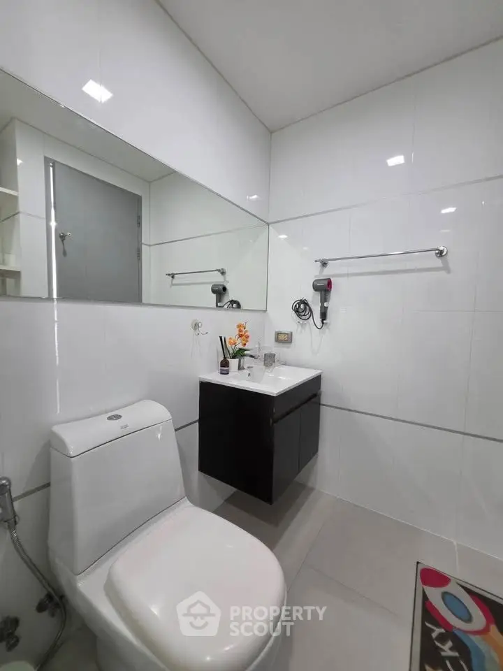 Modern bathroom with sleek fixtures and white tiles, featuring a wall-mounted sink and large mirror.