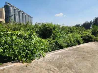 Expansive industrial land with lush greenery and silos, perfect for development opportunities.