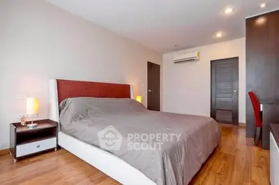 Spacious bedroom with modern decor and wooden flooring, featuring a comfortable bed and ambient lighting.