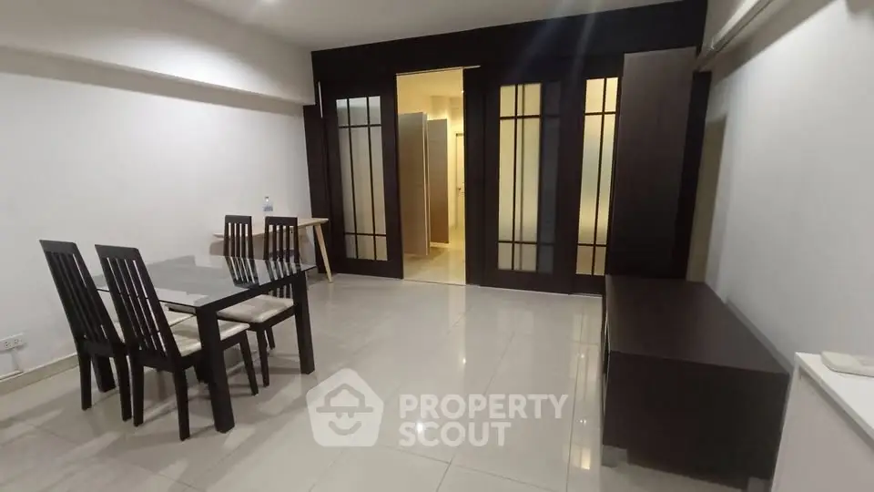 Spacious modern dining area with sleek glass table and elegant dark wood accents.