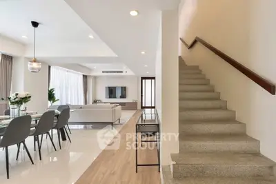 Spacious modern living room with dining area and staircase, featuring elegant decor and ample natural light.