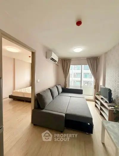 Modern living room with large sofa and natural light, adjacent to a cozy bedroom in a stylish apartment.