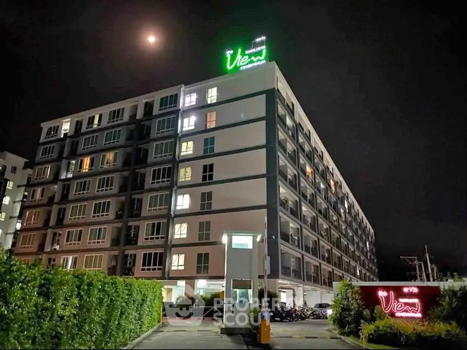 Modern apartment building at night with illuminated signage and lush greenery.