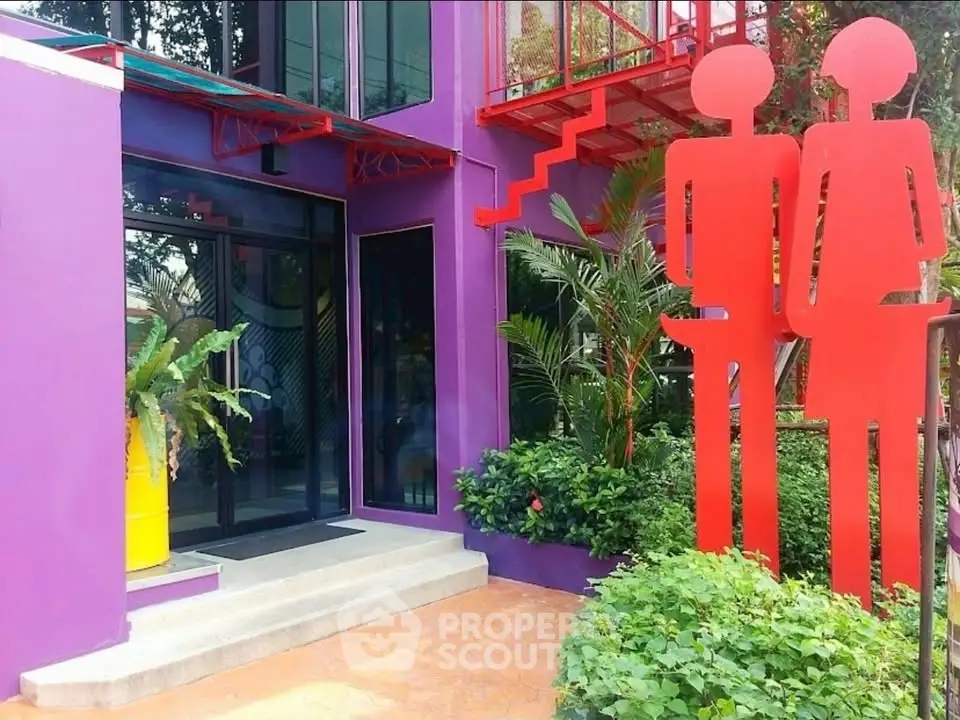 Vibrant purple building entrance with modern red sculptures and lush greenery.