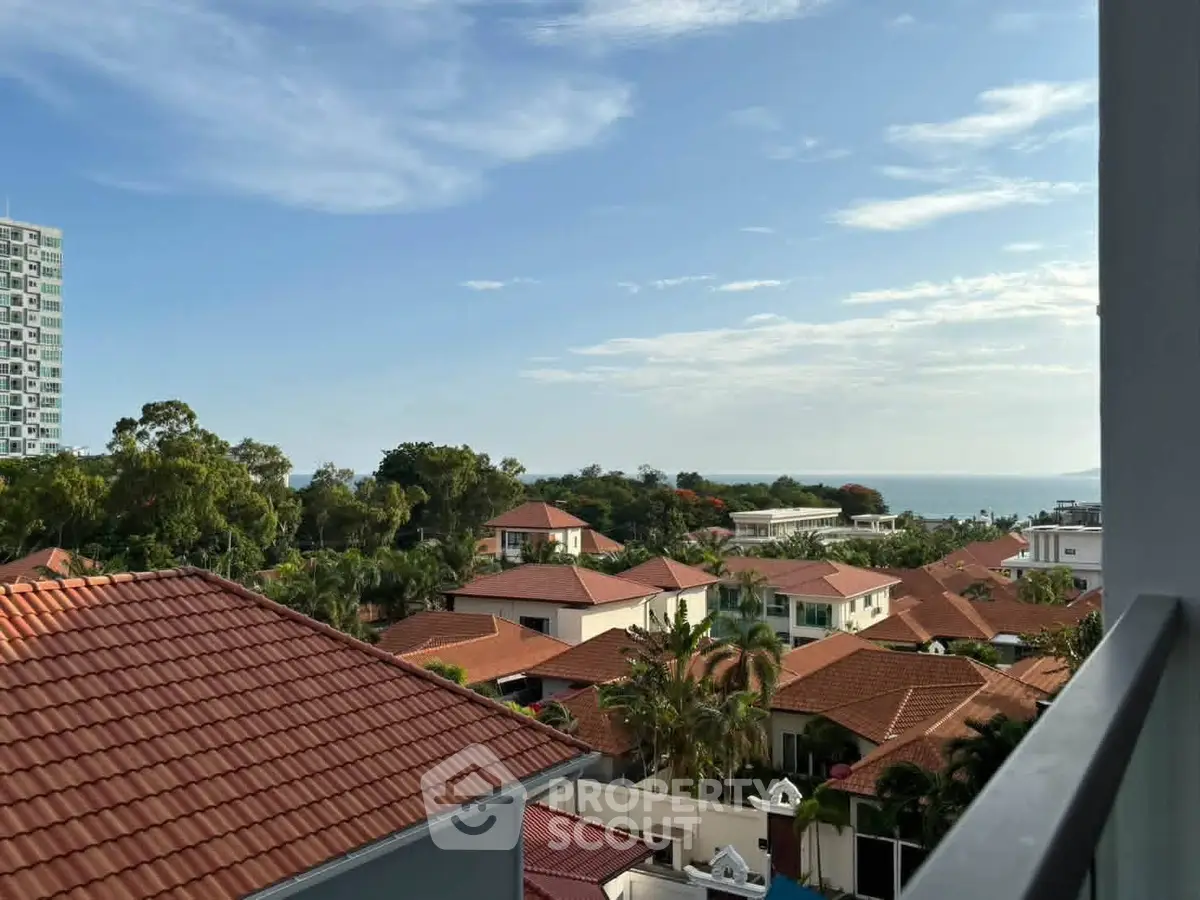 Stunning coastal view from a balcony overlooking red-roofed houses and lush greenery.