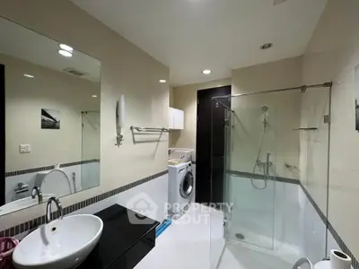 Modern bathroom with glass shower and washing machine in sleek apartment.