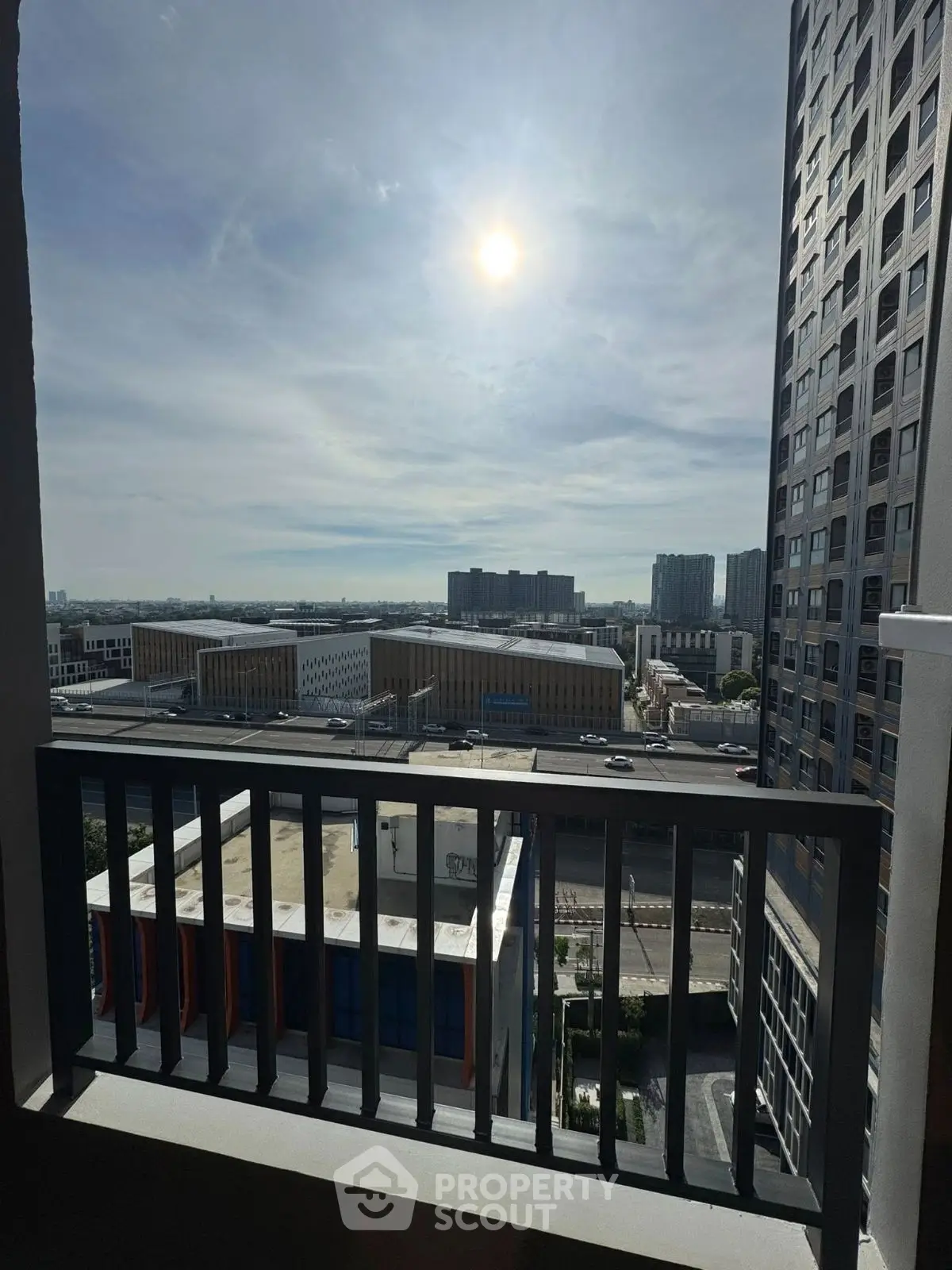Stunning urban view from a high-rise balcony with cityscape and sunlit sky.