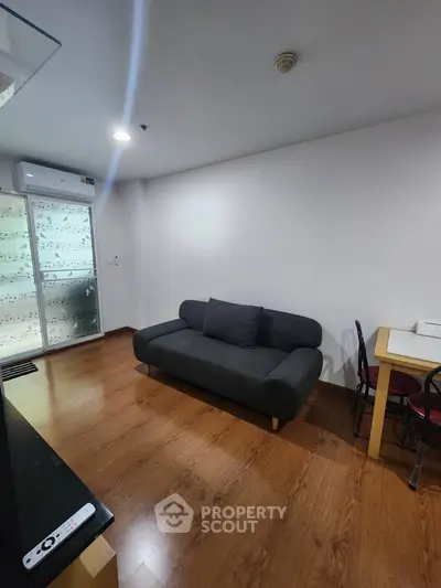Modern living room with sleek black sofa and wooden flooring, perfect for cozy relaxation.