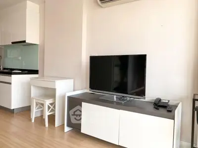 Modern minimalist living room with sleek white furniture, large flat-screen TV, and an open kitchen layout, perfect for urban living.
