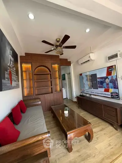 Charming living room with wooden furniture and modern decor, featuring a ceiling fan and air conditioning.