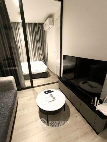 Modern living room with sleek furniture and glass partition leading to a cozy bedroom.
