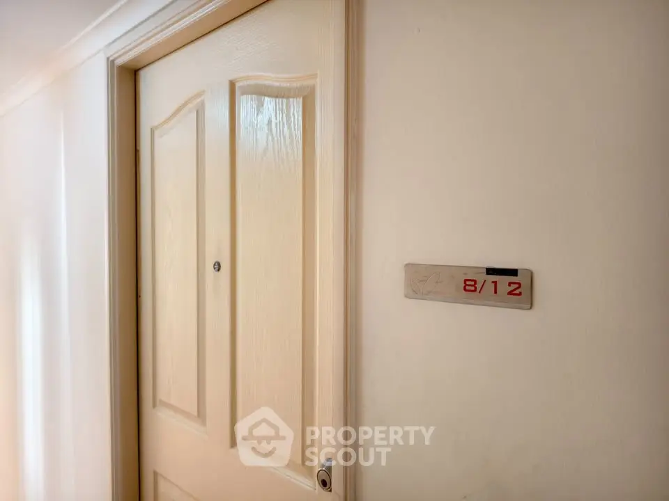 Apartment entrance with wooden door and unit number 8/12 on the wall.