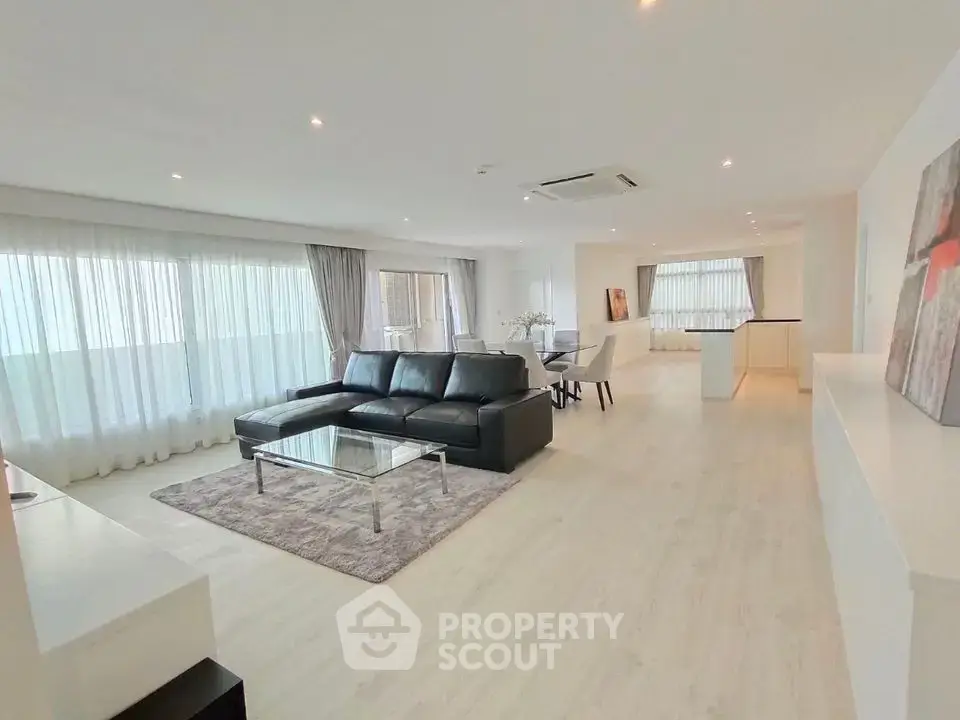 Spacious modern living room with sleek black sofa and large windows in a bright open-plan layout.