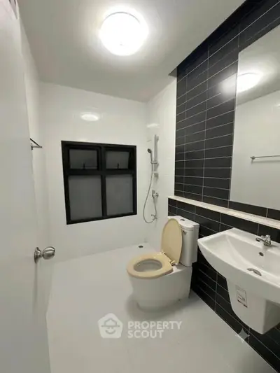 Modern bathroom with sleek black and white tiles, featuring a shower and contemporary fixtures.